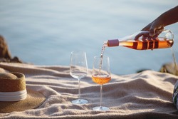 Woman hand pouring rose wine from bottle into glasses on the beach.