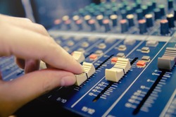 Audio mixer console and professional sound mixing. A hand is adjusting audio mixer with buttons and sliders. Mixer console for musician DJ and sound engineers.