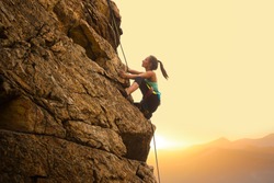 Beautiful Woman Climbing on the High Rock at Foggy Sunset in the Mountains. Adventure and Extreme Sport Concept