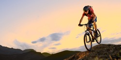 Cyclist in Red Riding the Bike Down the Rock in the Beautiful Mountains on the Sunset. Extreme Sport and Enduro Biking Concept.