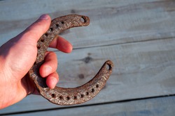 A man's hand holds an old horseshoe. Natural wood background. Place for your text.