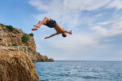 Freedom, motivation and creativity, man flipping from the scale on the beach. Young man doing a back flip into sea, Antalya, Turkey             