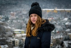 Half body portrait of beautiful Caucasian teenage girl at winter.
Pretty teen girl in snow, facing camera, blurred snowy city in background.
