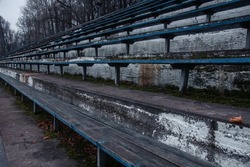 Concept of old buildings. Old stands of the city stadium in late autumn. Old wooden benches for spectators on the concrete base of the stands.