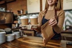 Cropped image, barista is working in coffee shop, young woman is standing behind the bar counter, making coffee, take away.