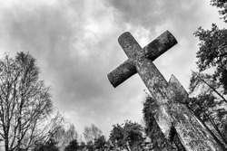 Ancient concrete cross in the cemetery against the background of the sky. Black and white image 