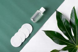 Make-up remover in small bottle and cotton discs on the green and white background. Cleansing skincare product