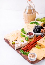 Cheese platter with assorted cheese, sausage, jam, black olives, pine nuts and grapes. Appetizer variation and bottle of white wine