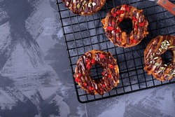 Donut shaped cakes with caramel, chocolate, goji berries and pumpkin seeds on the cooling rack on gray table. Top view. Dessert variation