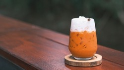Thai Milk Tea, Milk ice tea, Cheddar is a traditional Thai drink that has long been popular, fresh and sweet dessert on a wooden saucer, vintage wooden table in cafe.