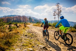 Mountain biking woman and man riding on bikes at sunset mountains forest landscape. Couple cycling MTB enduro flow trail track. Outdoor sport activity.