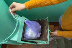A woman's hand with a garbage bag opens the hatch of the garbage chute and throws garbage there. Top view