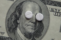The pills lie in place of the eyes, on a bill of one hundred dollars close-up. The concept of insurance medecine, insurance, high cost, high cost of drugs.