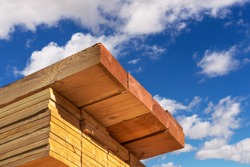 Stack of dimensional lumber for home construction with partly cloudy sky. 