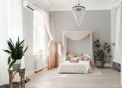 Modern bedroom with tester bed with pale pink tester and pale pink folding-screen, small accent pillows on the bed, minimalistic Scandinavian design bedroom with indoor plants and light grey walls.