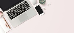 bright feminine banner / header with a stylish workspace with laptop computer, smartphone modern office accessories and a small succulent on a blush table, top view / flat lay