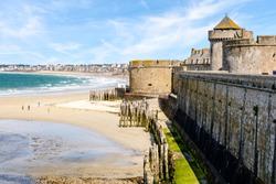 The city of Saint-Malo in Brittany seen from the surrounding wall of the old town with the towers of the castle, the breakwater made of wooden posts and the beach of L'Eventail on a sunny day.