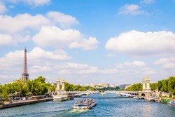 Cityscape of Paris, France, with a bateau-mouche cruising on the river Seine, the Alexandre III bridge, the Eiffel tower on the left and the Chaillot palace in the distance by a sunny summer day.