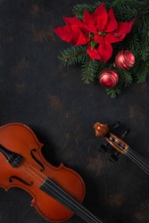 Old violin and fir-tree branches with Christmas decor and poinsettia.  Christmas and New Year's concept. Top view, close-up on dark concrete background.
