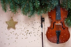 Old violin and fiddlestick, fir-tree branches with Christmas decor. Christmas, New Year's concept. Top view, close-up on pastel color background	