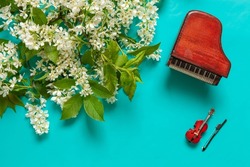 Miniature piano and violin with blooming wild cherry tree branches. Top view, close-up on light blue background