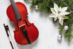 Old violin and fir-tree branches with Christmas decor and white poinsettia. Christmas, New Year's concept. Top view, close-up.	