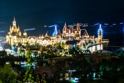 Glowing buildings in amusement park at night with funicular over sea
