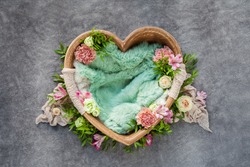 brown wooden bowl in the shape of a heart for newborn babies on a grey background with a green woolen rug, carnations, eustomas, roses and green twigs