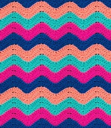 Seamless knitted pattern in the form of zigzags is crocheted with multi-colored threads. Acrylic baby yarn. Colorful background.