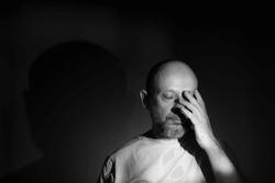 Black and white portrait of depressed middle age man with hand on face isolated on black background having financial problems or suffering from loneliness