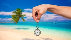 Hand holds a clock on the background of an exotic beach