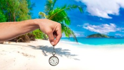 Hand holds a clock on the background of an exotic beach