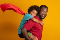 African Father and Son playing Superhero at the day time. People having fun yellow background. Concept of friendly family.