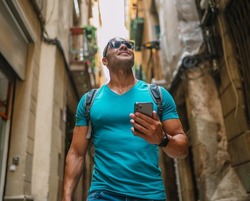 Happy male tourist phone user walking in old town alley an using smartphone. GPS maps, concept. Barcelona, Spain.