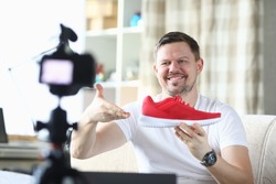 Man shows red sneaker in front camera, video blog. Quality product description. Guy works remotely, offering goods online. Man in his apartment takes an overview new sports shoes