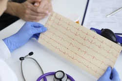 Doctor's hands hold result of the cardiogram next to patient sitting. Examination of the cardiovascular system concept.