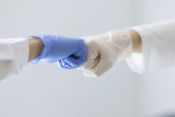Doctors in rubber gloves touching their fists in clinic close-up. Health care workers cooperation concept