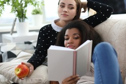 Two women on couch are reading book