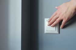 Female hand pressing light switch in apartment closeup