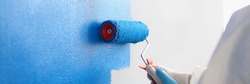 Repairman painting white wall in apartment blue using roller closeup
