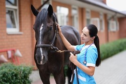Female doctor in uniform with horse in stable