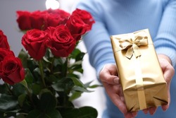 Bouquet of red roses and golden gift box in hands of courier