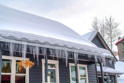 Gabled roof of home covered with thick snow and lined with icicles in winter