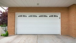 Panorama White sectional garage door with glass panels at the top. Exterior of a house with brown bricks siding and a concrete driveway at the front of the garage.