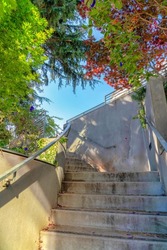 Weathered beige concrete outdoor staircase in San Francisco, California. Low angle view of a stairs with wall-mounted handrailing on the left.