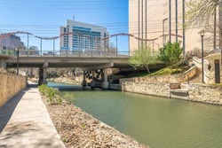 Walkway beside the river near the bidge and buildings at San Antonio, Texas. Concrete walkway with lamp posts and a view of a staircase on the right near the bridge and mid-rise buildings at the back.