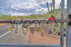 Tucson, Arizona- Multiple padlocks with chains on a gate. Close-up of multiple gate padlocks against the concrete pathway in the middle of desert landscape.