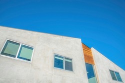 La Jolla, California- Building with off-white and wood cladding wall. Low angle view of a building with sliding windows and clear glass panes and a clear blue sky background.