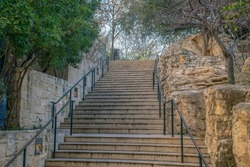 Outdoor stairway by the San Antonio River Walk in Texas on a beautiful day. The concrete steps with railings is flanked by stone half walls and small trees.