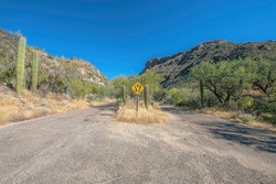 Hiking trail with paved roads and signage against mountain and blue sky. The scenic Sabino Canyon recreation area on a sunny day in Arizona state park.